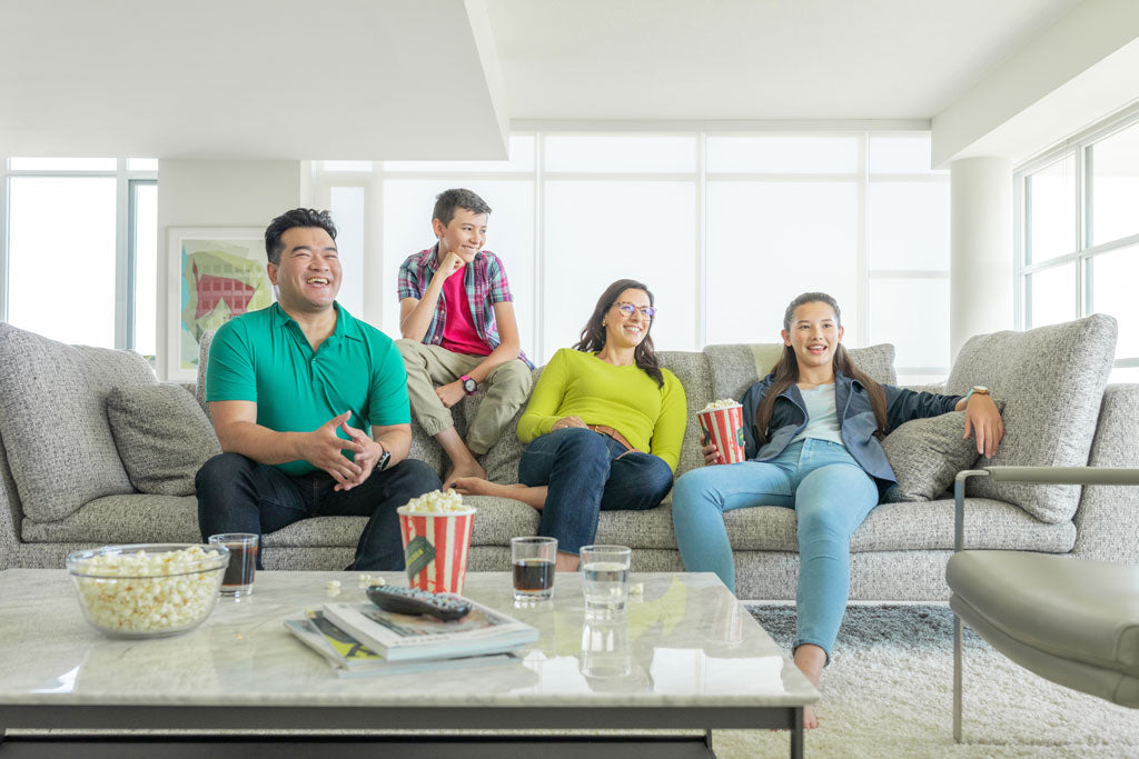 A Family Sitting On A Couch, Eating Popcorn, And Watching TV