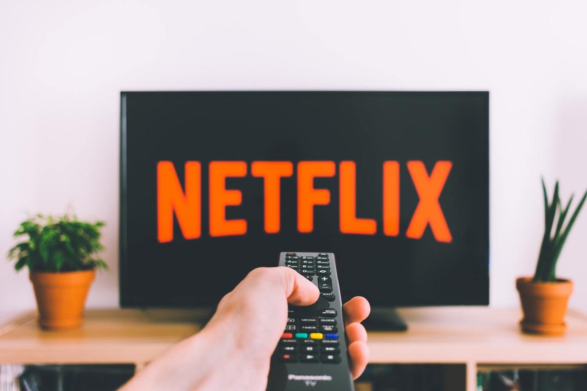 Netflix Streaming On TV, Hand Holding TV Remote Pointed At The TV