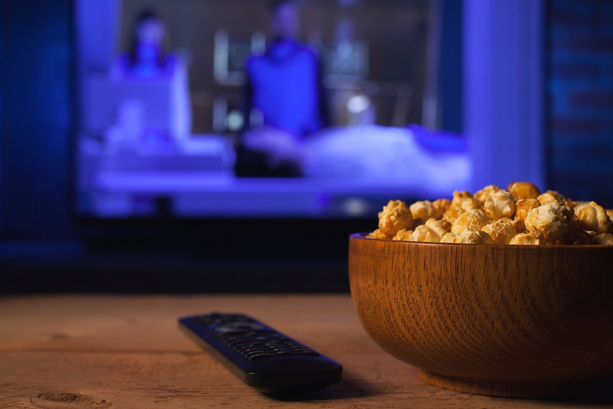 Wooden Bowl Of Popcorn And TV Remote, With A Blurry TV In The Background