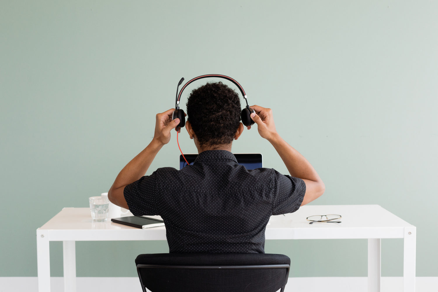 Person at a desk putting on headphones in front of a laptop, preparing for customer support.