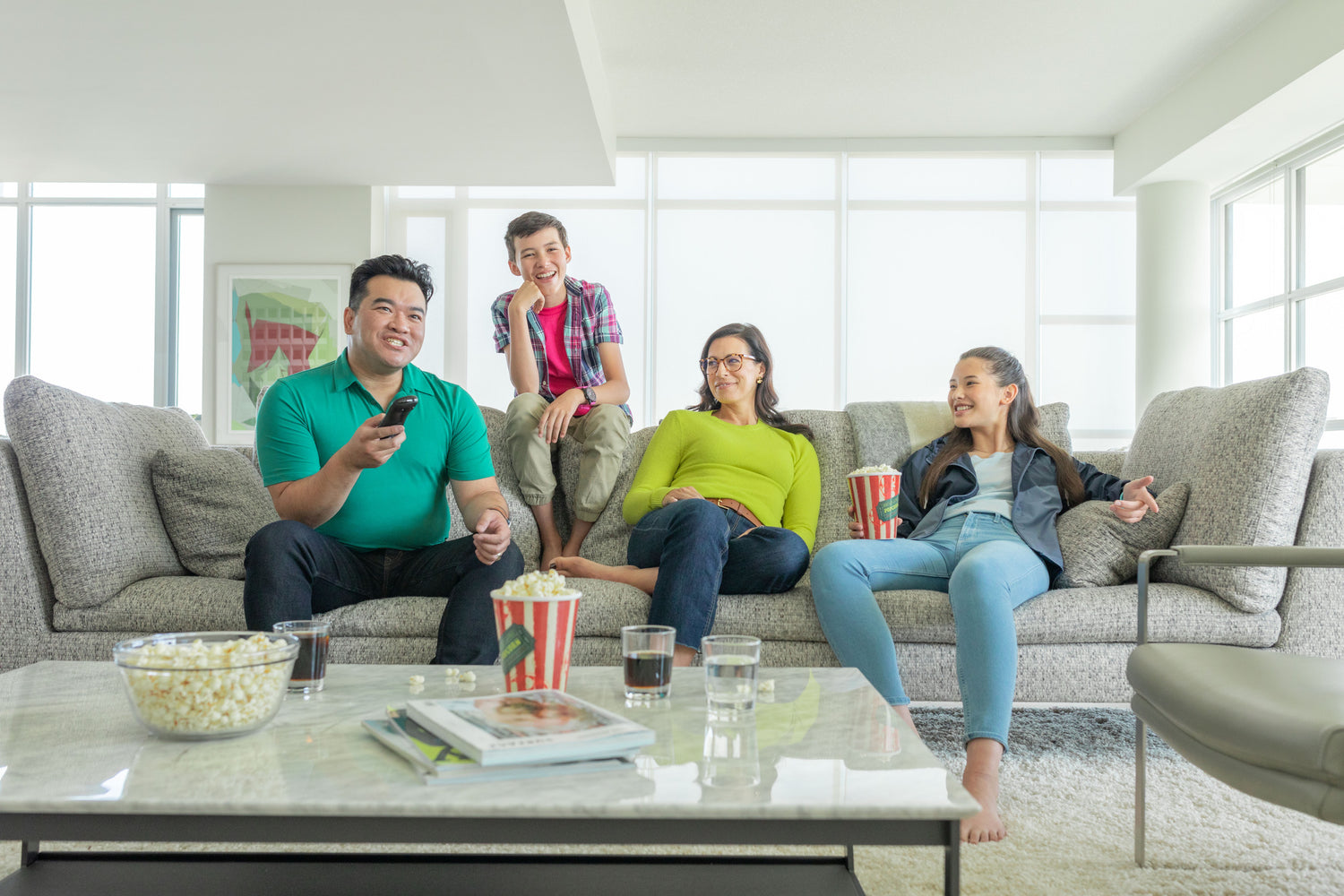 A Family Sitting On Couch, Eating Popcorn, And Watching Tv